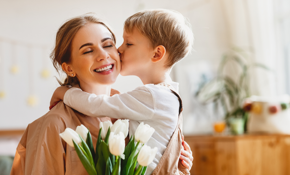 A tender young son kissing his mother on her cheek, they both look very happy