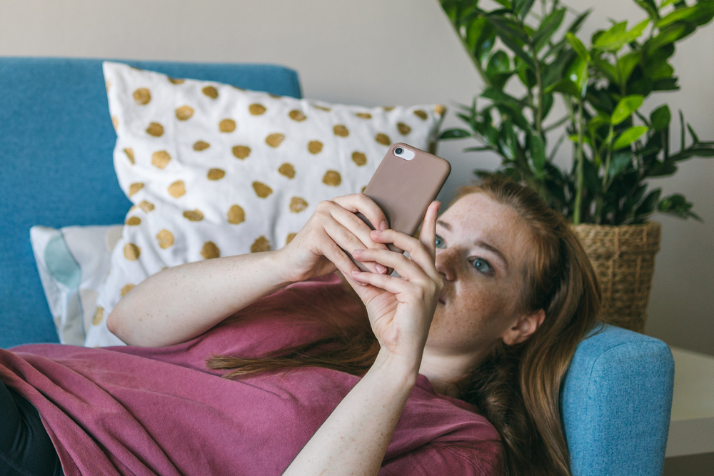 A sad young woman looks into her phone