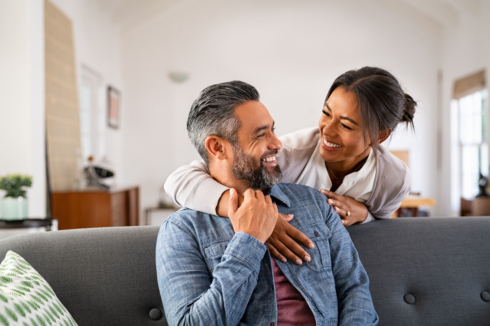 A smiling mature woman and her husband sitting on the couch in the living room