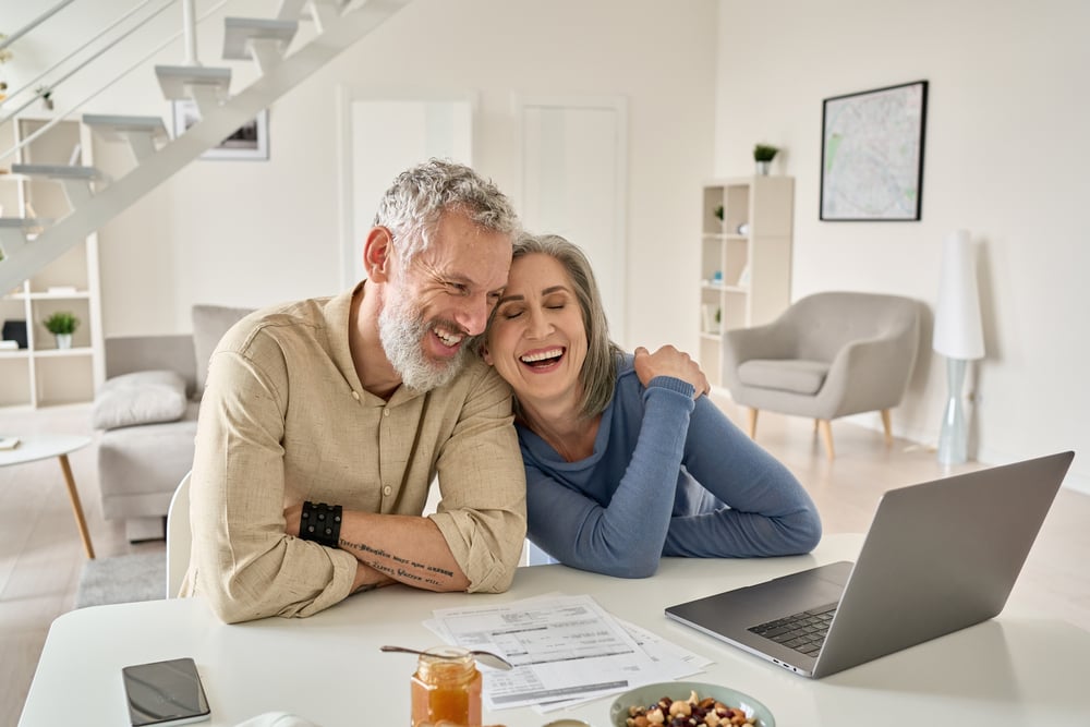A happy mature older couple having a laugh while spending time together and looking at the laptop screen before them