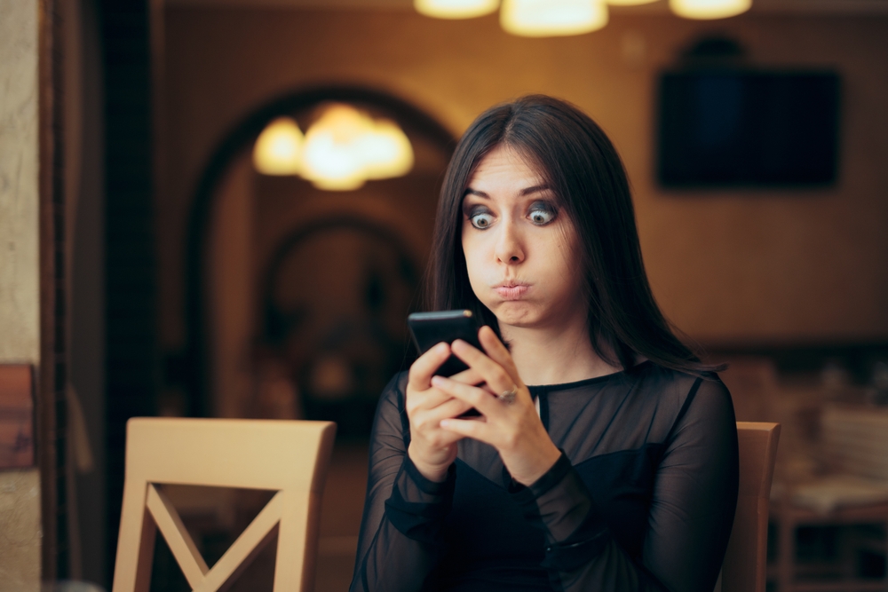 Surprised young woman sending a text from her phone
