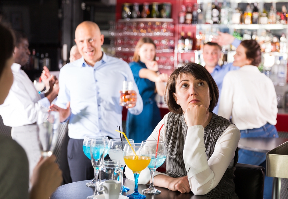 Bored woman sitting at table among dancing colleagues at corporate function
