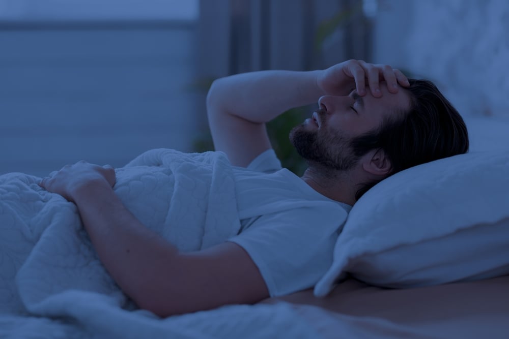 A sleepless young man in bed alone and thinking with his right hand on his forehead