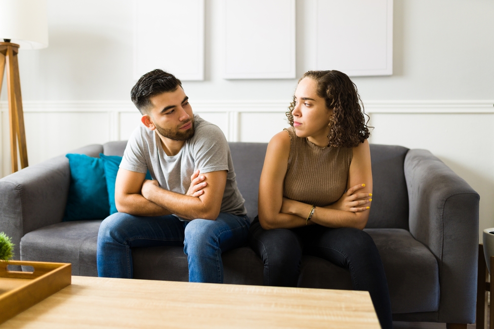 An angry couple sitting on the couch, distant from each other