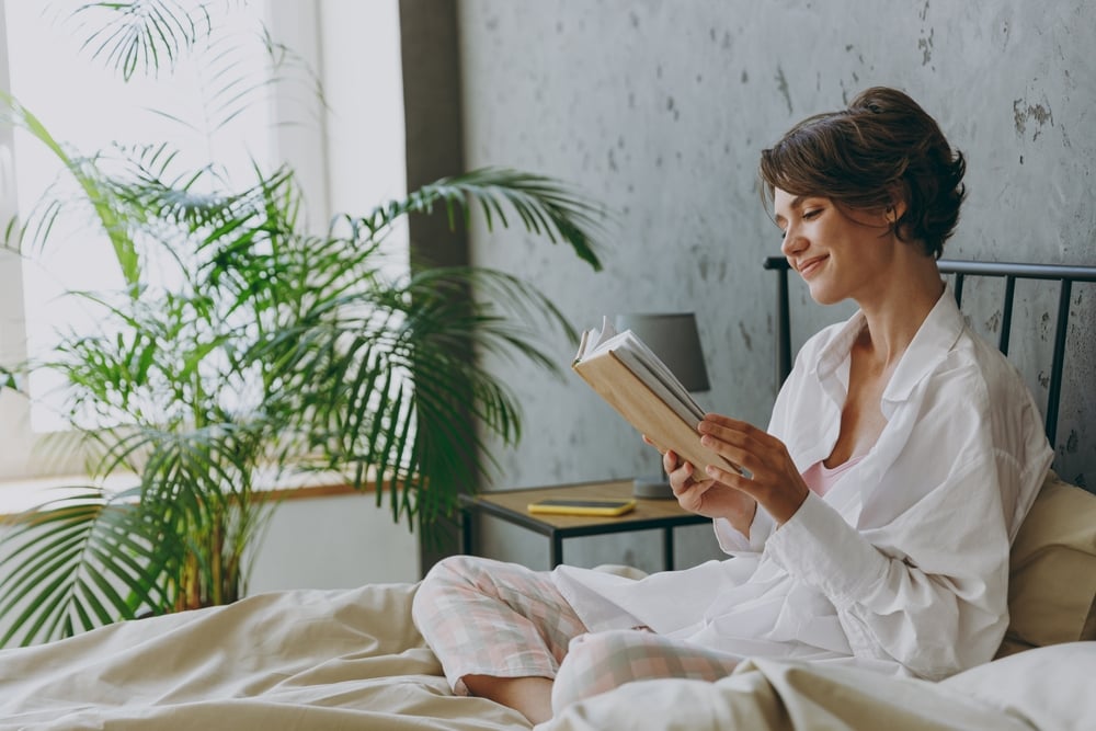 A young calm happy woman reading a book in bed
