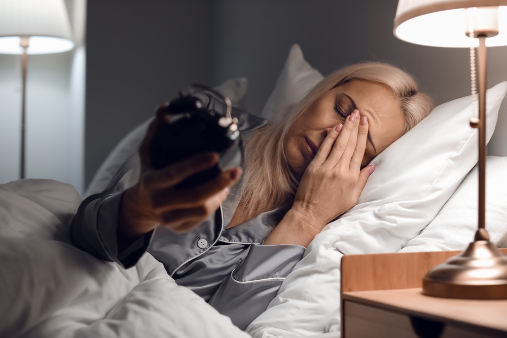 A stressed mature woman just waking up and looking at the alarm clock