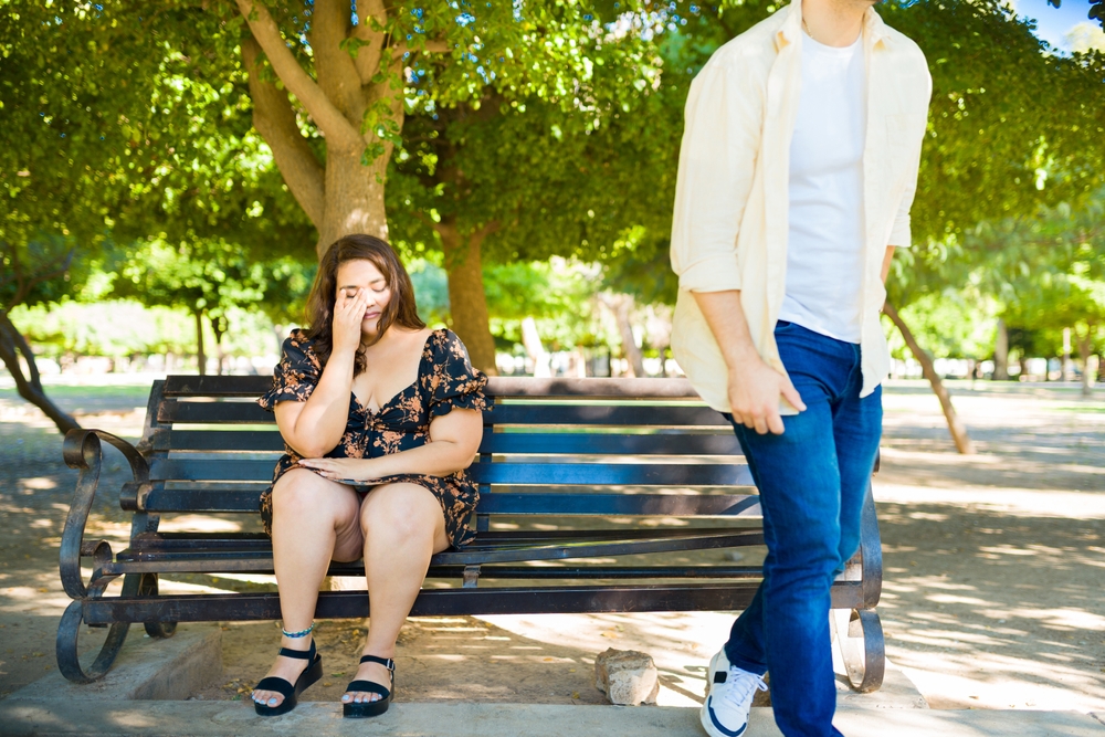 Boyfriend breaks up with his girlfriend and walks away, girlfriend remains sitting on a park bench and begins to cry