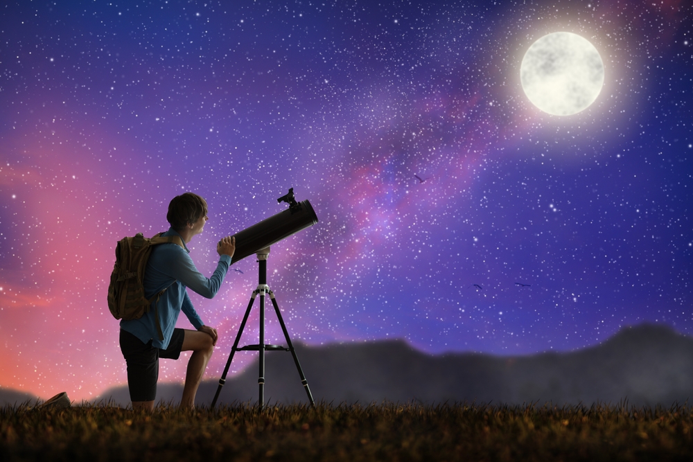A young man looking through a telescope at the stars.