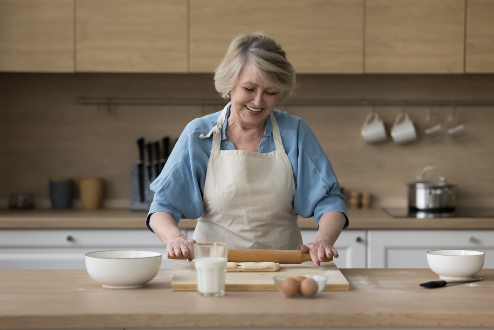 A happy senior woman cooking in the kitchen alone and kneading dough