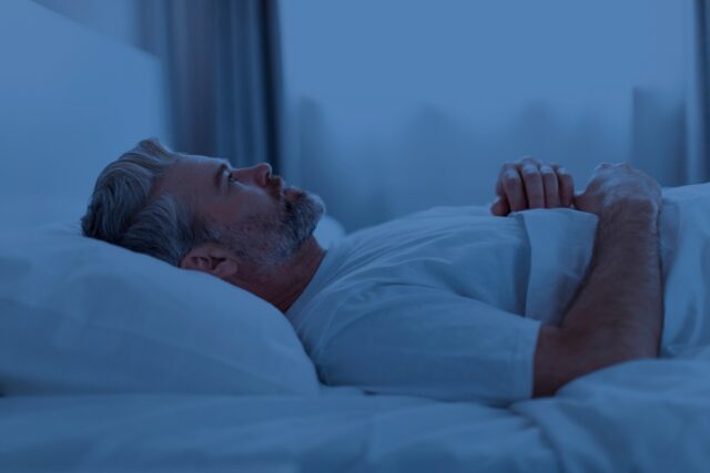 Man lying awake in bed, having trouble falling back to sleep.