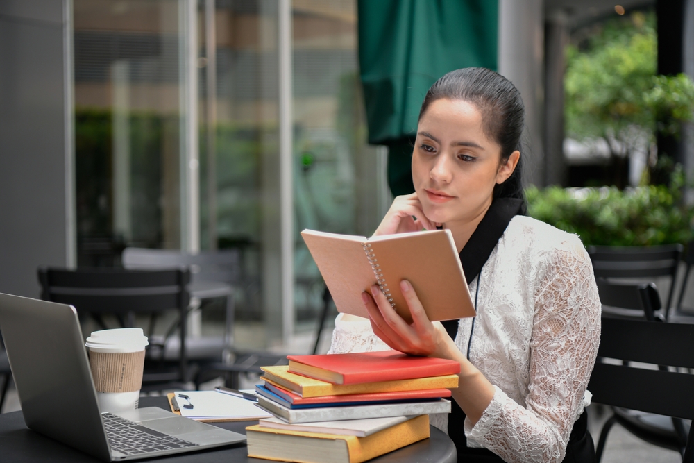 A young woman reading a book among a stack of books
