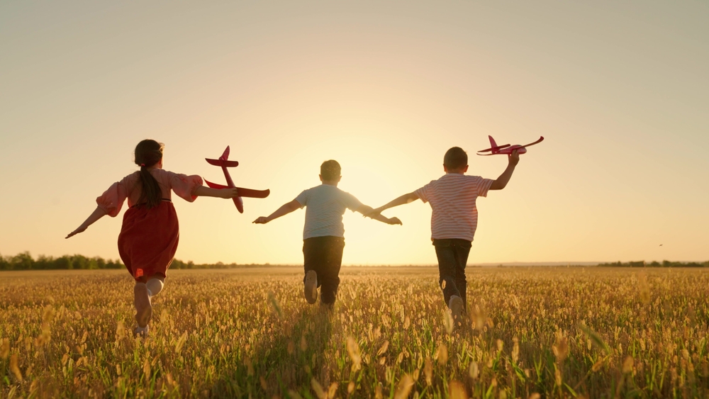 Happy children running outside as the sun sets with kites.