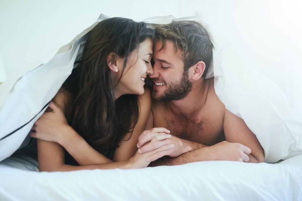 A smiling young couple in love in bed, under the covers