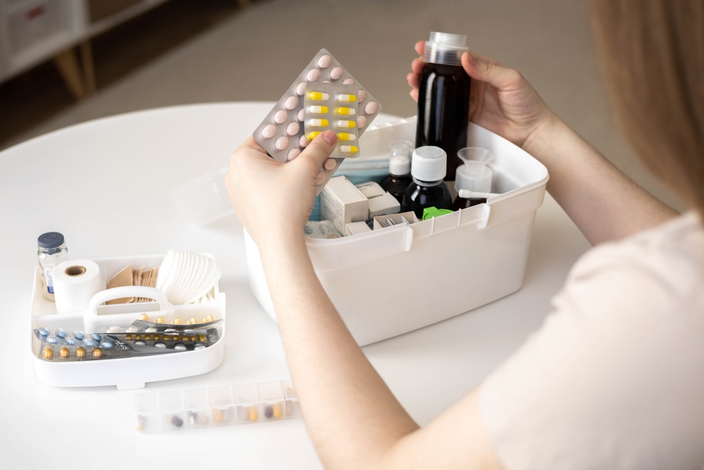 A female hand neatly placing medications in a white domestic first aid box