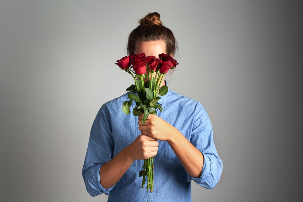 Shy woman holding roses over her face.