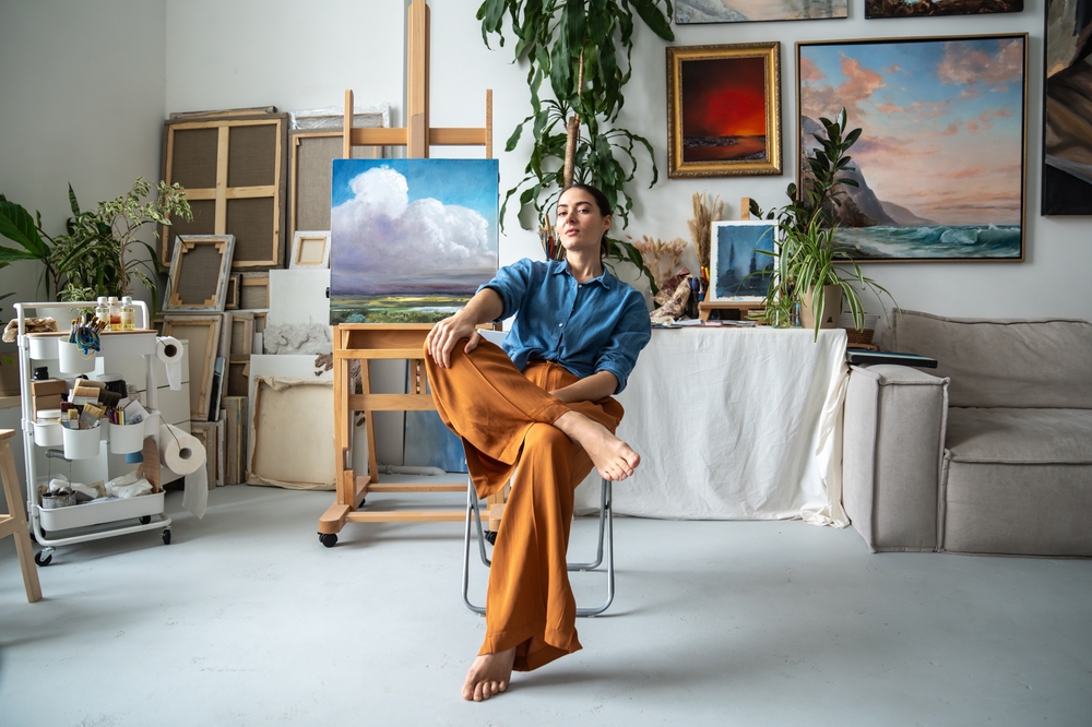 A proud, confident female artist in her studio in front of her paintings