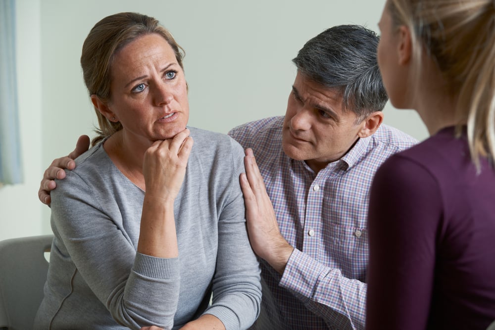 Mature couple talking to a therapist while the husband tries to comfort the wife