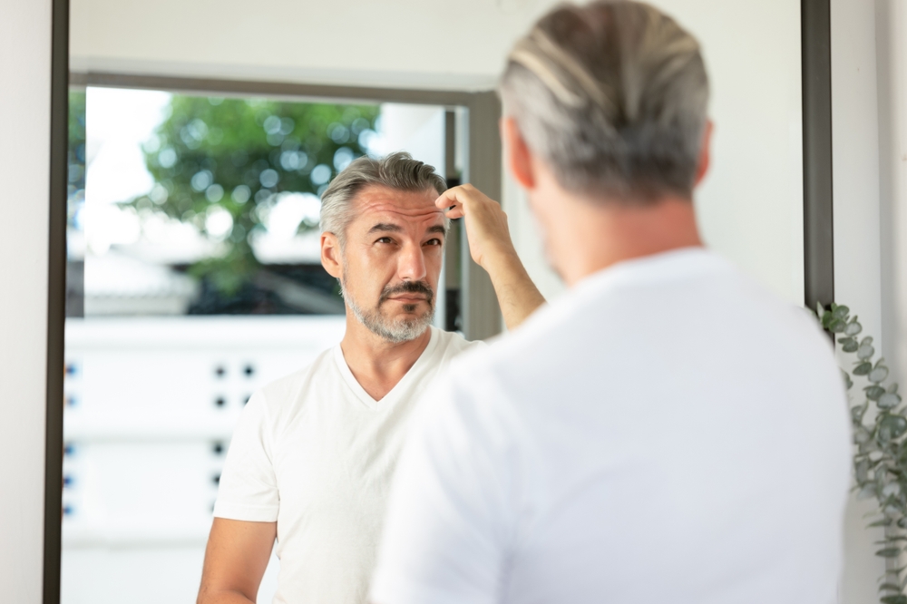 A handsome mature grey haired man looking in the mirror and arranging his hair