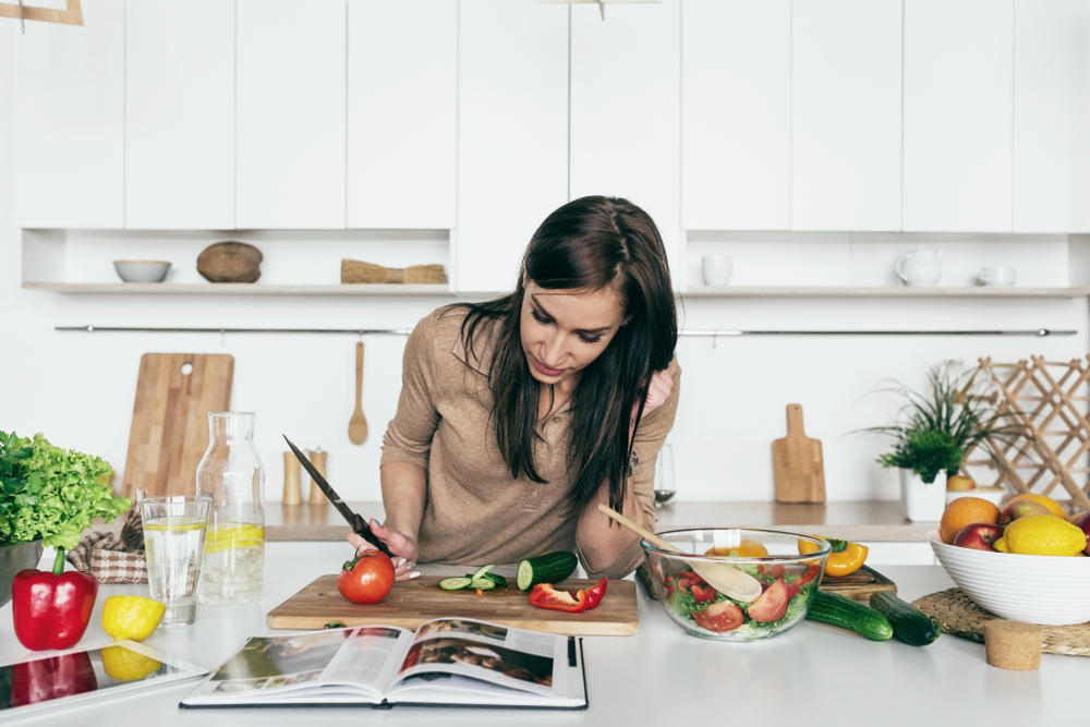 A woman reading recipe from a cookbook as she cooks