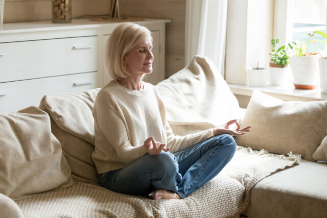 A mindful middle age woman sitting on the couch and meditating.