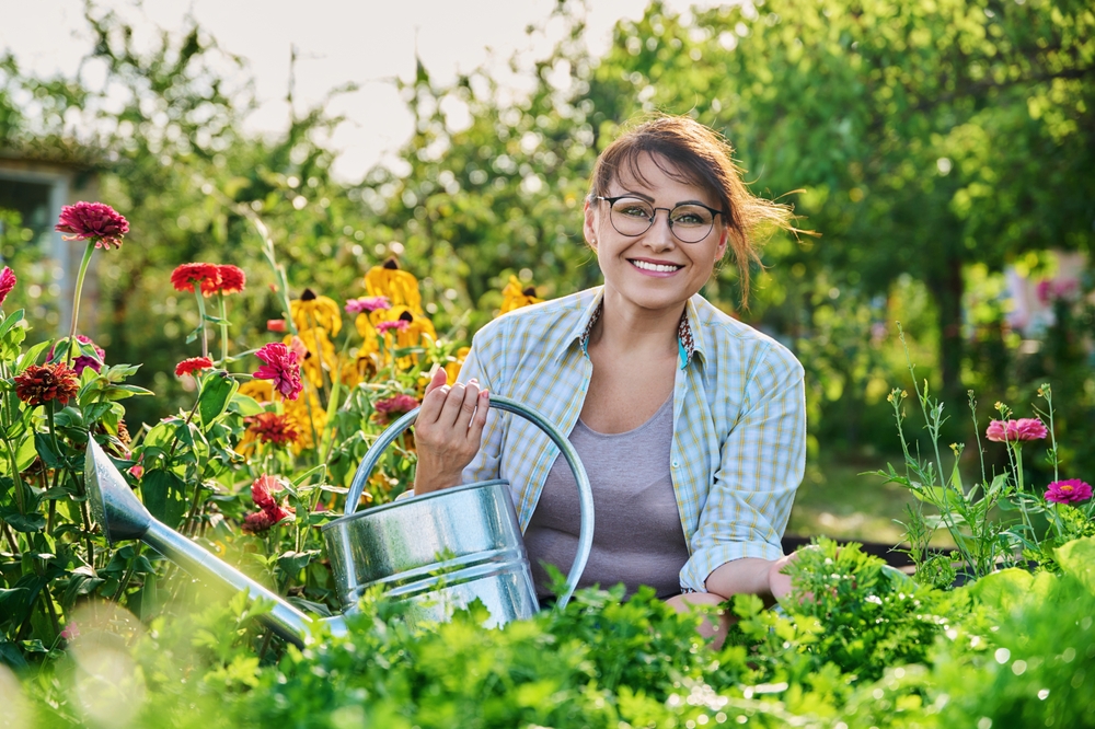 A middle aged woman in a garden with her watering can