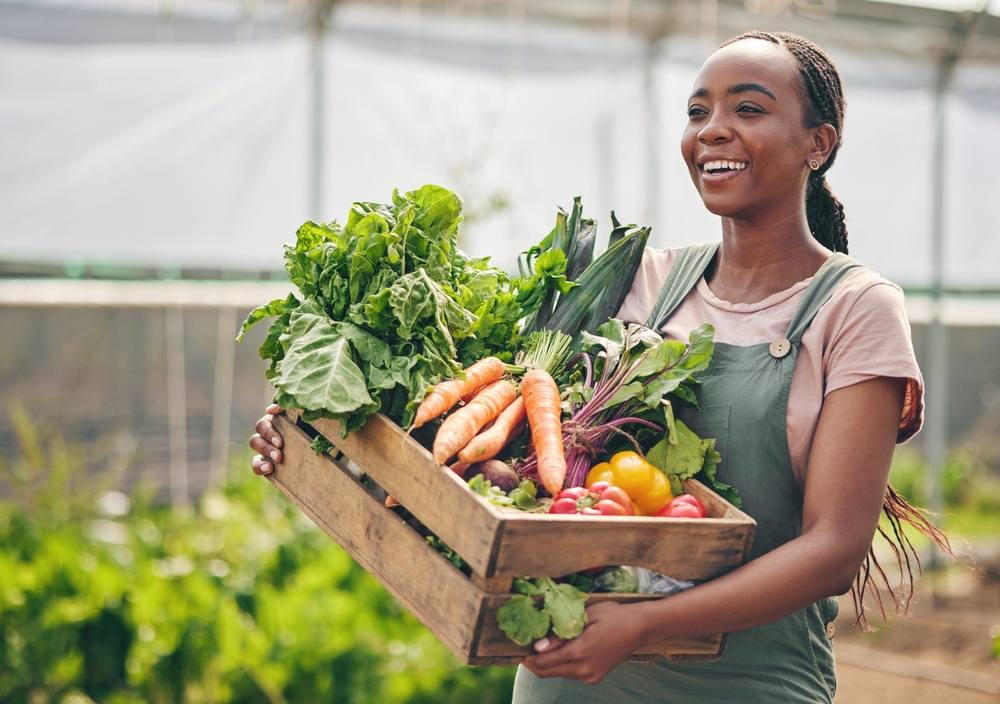 A young black female farmer carrying her harvested fresh vegetables and carrots