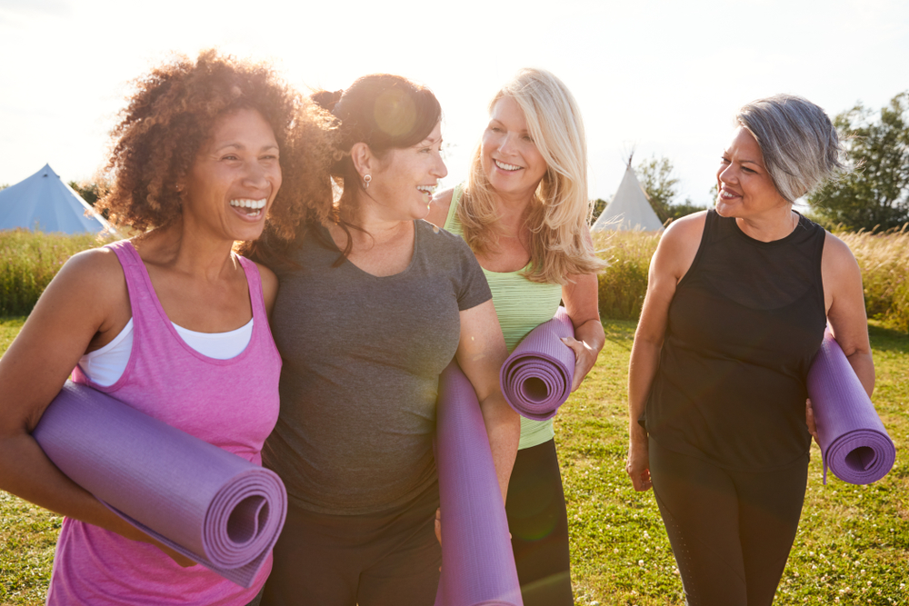 Four mature middle age women going for a yoga session with their yoga mats tucked under their arms