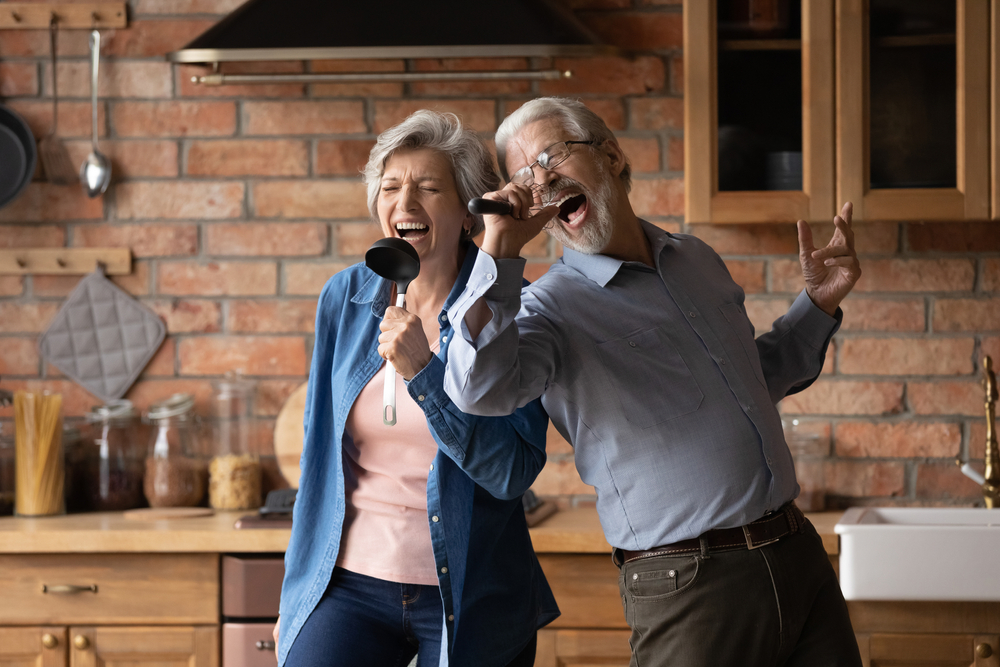 Happy senior husband and wife have fun and sing in the kitchen