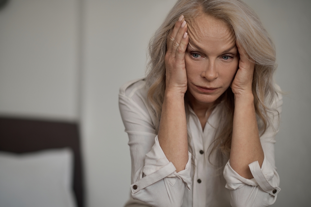 A mature blond woman looks despondent and holds her head with both hands