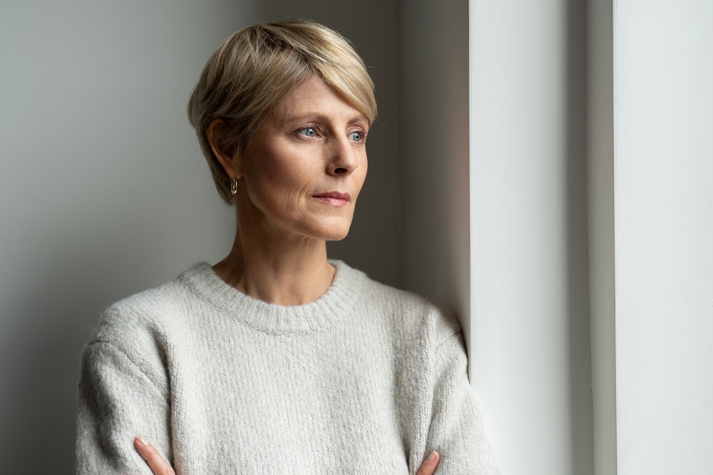 A sad middle aged woman with short blond hair looking out the window, lost in thoughts