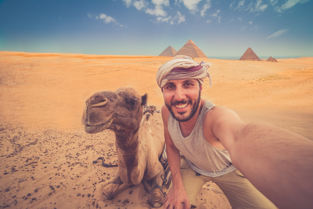 A happy tourist riding a camel and taking a selfie while on vacation.