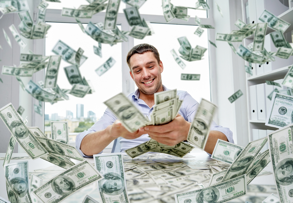 A young successful business man spraying cash while sitting