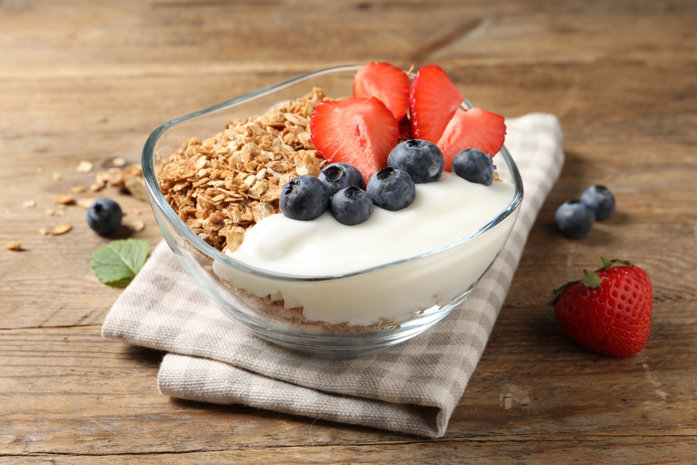 A glass bowl filled with granola, yogurt and fresh berries.