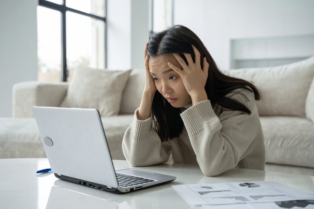 A tired and exhausted Asian woman looking at her laptop screen