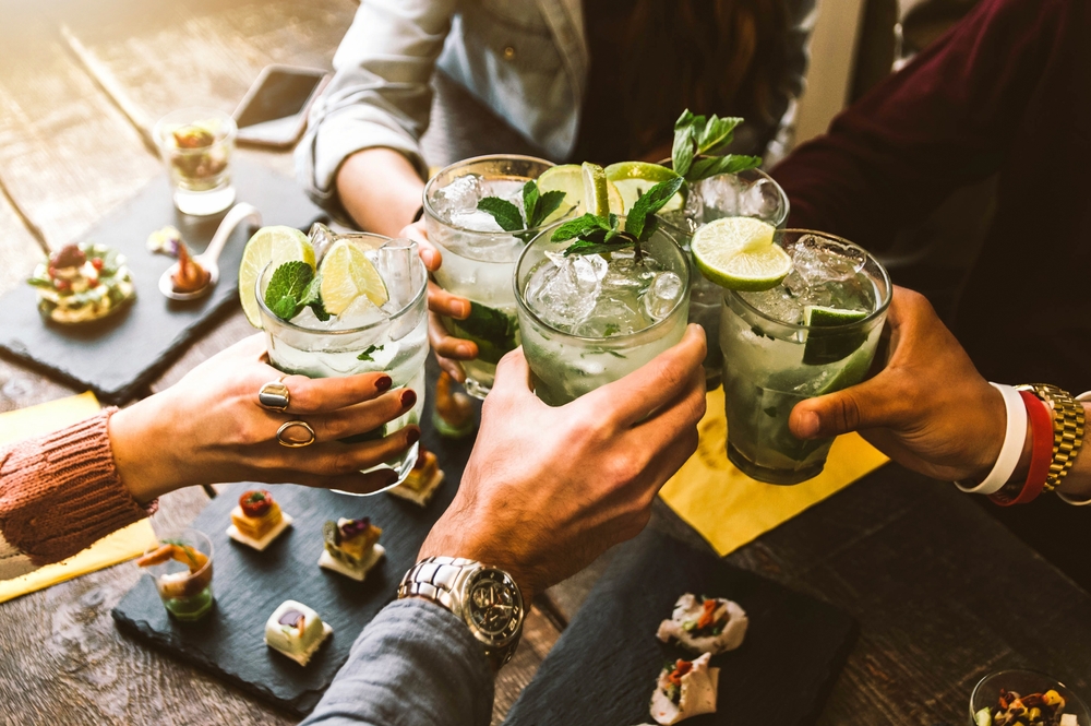 Happy group of friends cheering at a bar with mojito drinks