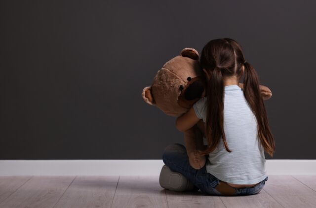 small girl sitting alone hugging large teddy bear