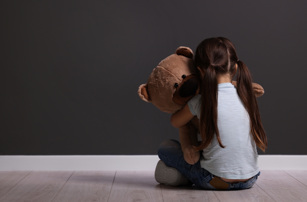 small girl sitting alone hugging large teddy bear