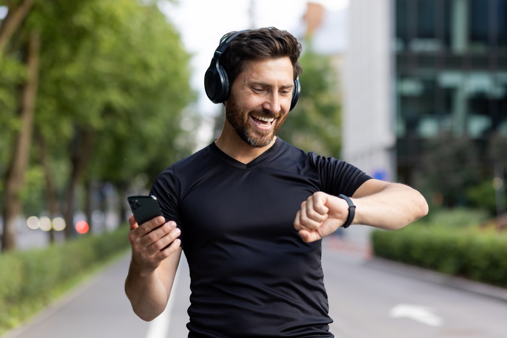 A happy middle age man going on a fitness walk checking his watch, with headphones on his head