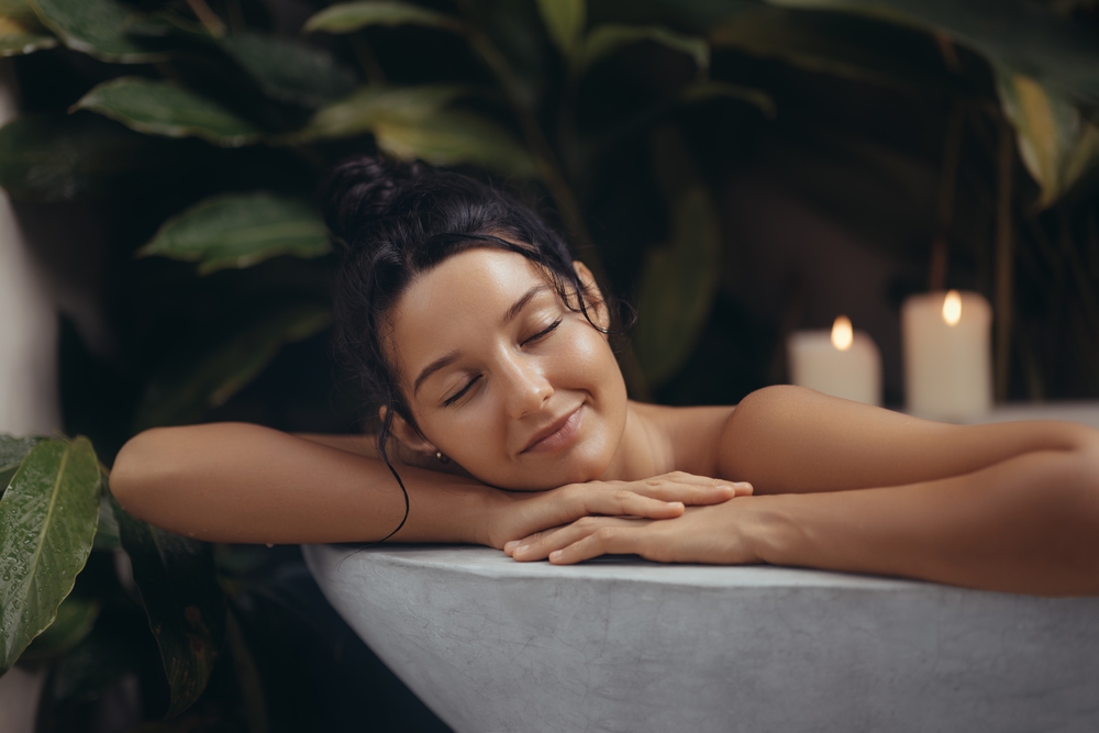 A serene young woman having a soak in her bathtub, she has a relaxed expression on her face