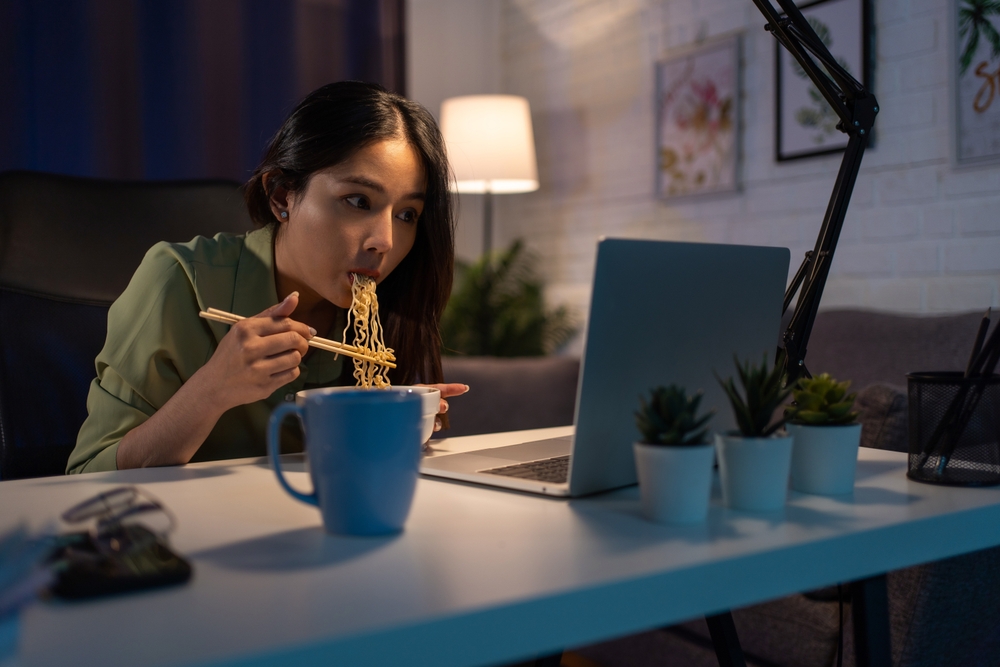 An Asian young woman eating noodles and watching movies on her laptop