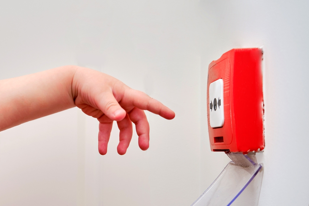 Child's hand reaching for a fire alarm.
