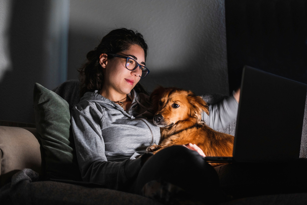 A woman watching a movie with her laptop while cuddling with her dog
