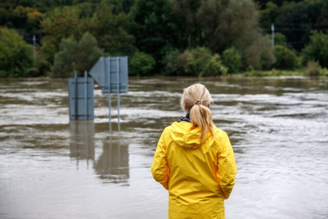 Woman standing in yellow raincoat, viewing the recent flood event.