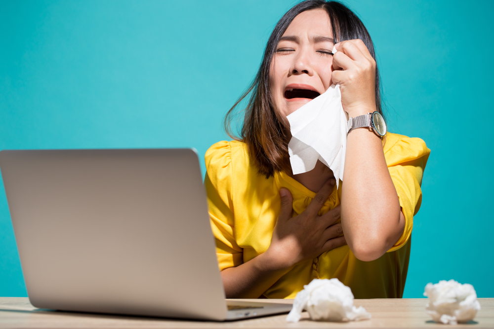 Woman crying with her laptop in front of her, cleaning her tears with a napkin
