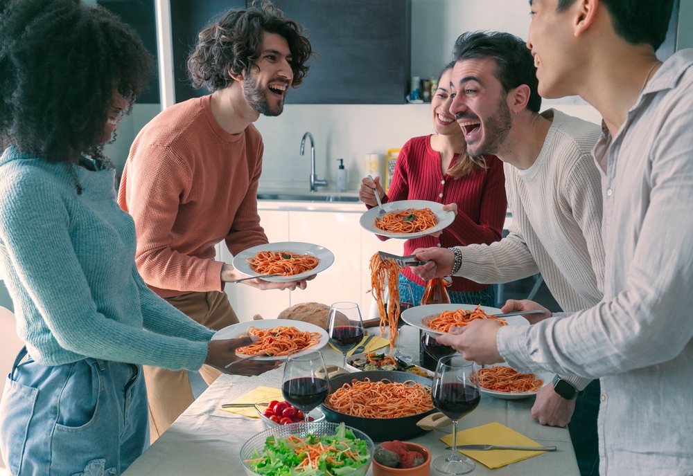 A group of friends having dinner together at home. The host, a man, is serving pasta to his friends