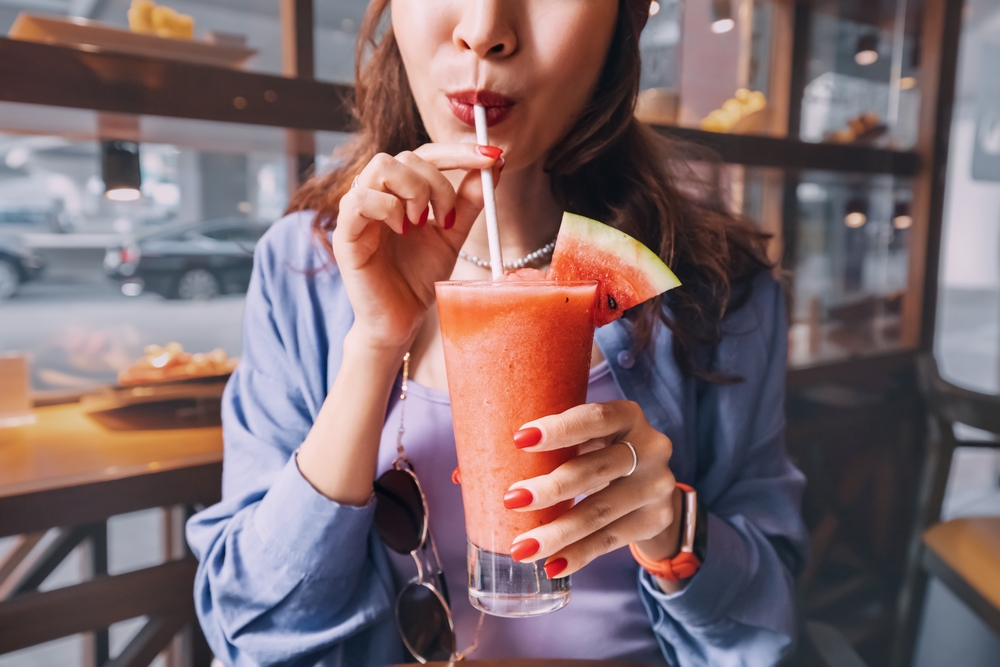 A woman sipping with her straw on a watermelon smoothie at a cafe
