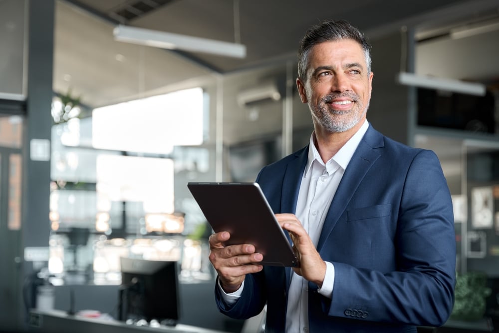 A Happy middle aged businessman wearing a suit, standing and holding a tablet