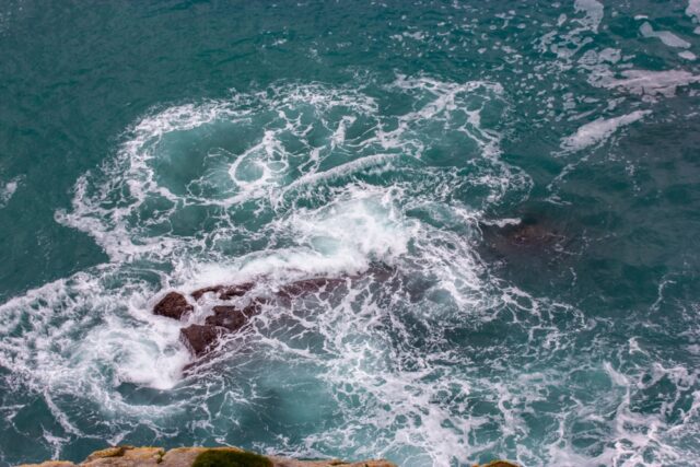 A raging ocean with a funnel, vortex of blue water viewed from a cliff. Rocky coastline.