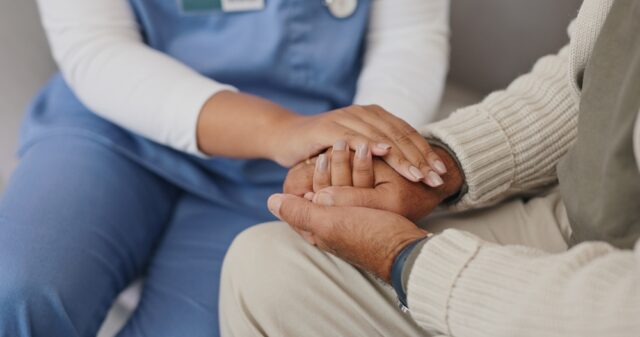 Nurse offering comfort while holding hands with an elderly patient.