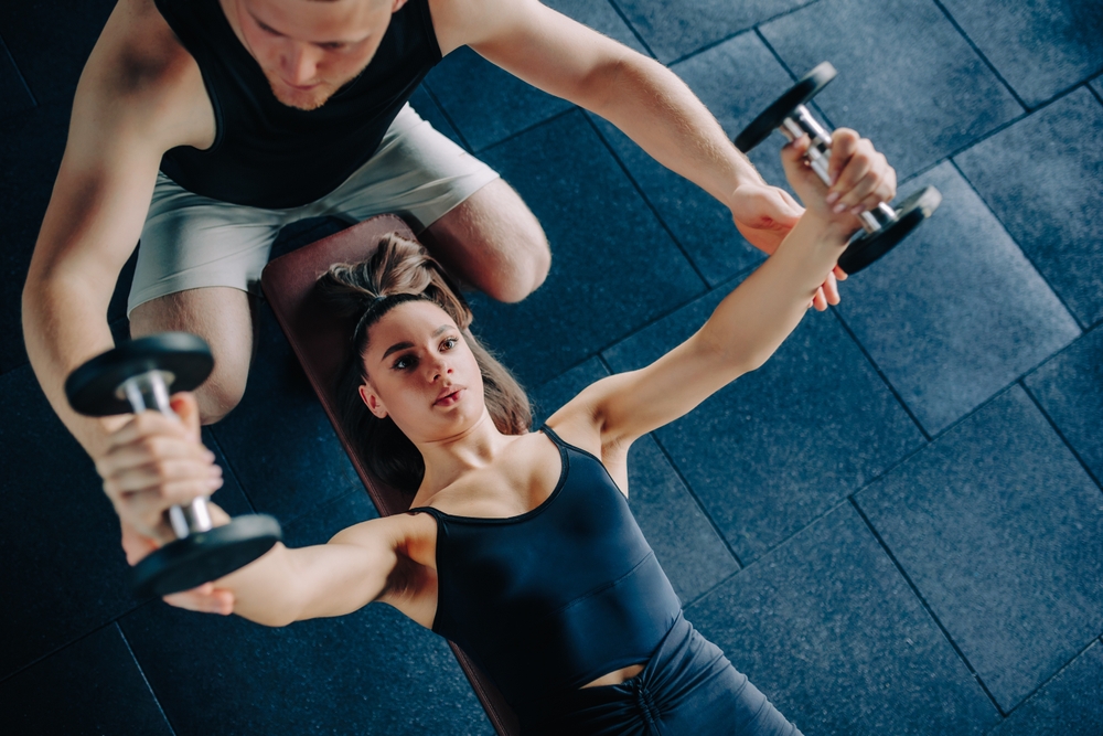 Male Personal trainer working with his female client, using weights in the Gym